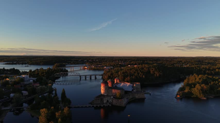 High aerial view of medieval Olavinlinna Castle illuminated by golden hour sunset light on Lake Saimaa in Savonlinna, Finland.