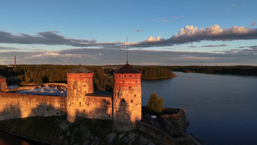 High aerial view of medieval Olavinlinna Castle illuminated by golden hour sunset light on Lake Saimaa in Savonlinna, Finland.