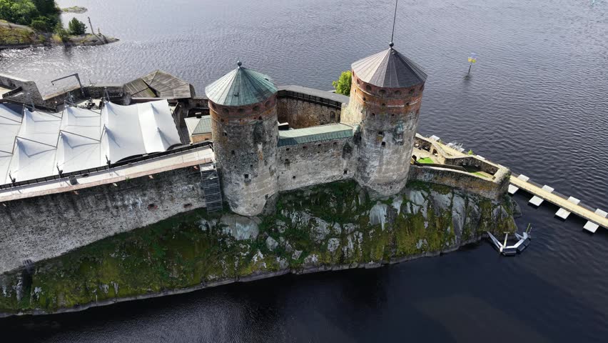 Aerial panoramic view of medieval Olavinlinna Castle surrounded by Lake Saimaa under a blue sky in Savonlinna, Finland.