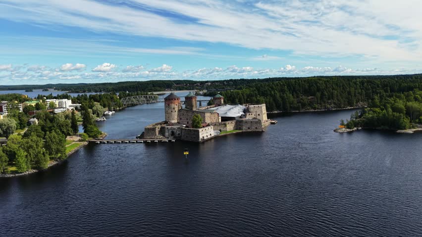 Aerial panoramic view of medieval Olavinlinna Castle surrounded by Lake Saimaa under a blue sky in Savonlinna, Finland.