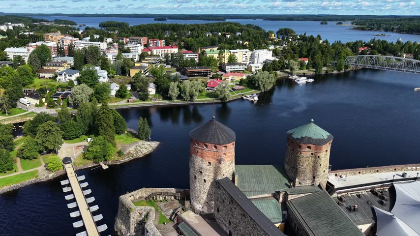 Aerial panoramic view of medieval Olavinlinna Castle surrounded by Lake Saimaa under a blue sky in Savonlinna, Finland.