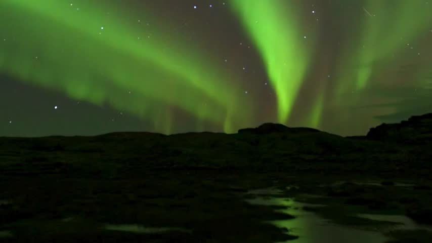 Breathtaking vertical video of vibrant green aurora borealis illuminating the night sky with bright stars over dark terrain.