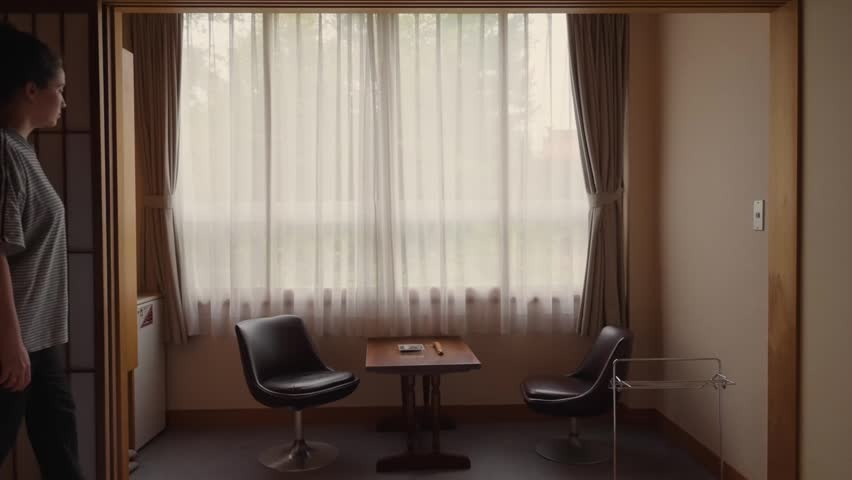 Young woman waking up in a traditional Japanese ryokan hotel room in Hokkaido, opening the curtains to look at the lush green forest outside the window, starting a new day on vacation