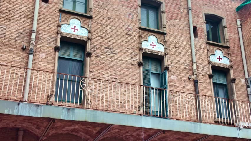 Hospital de Sant Pau features exposed brickwork, wrought iron balconies, ornamental window surrounds and decorative ceramic crosses in Barcelona, Spain, emphasizing its Modernist architectural details