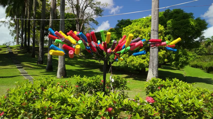 Colorful handmade decor tree sculpture made from painted tubes standing among palms at Scarborough Botanical Garden