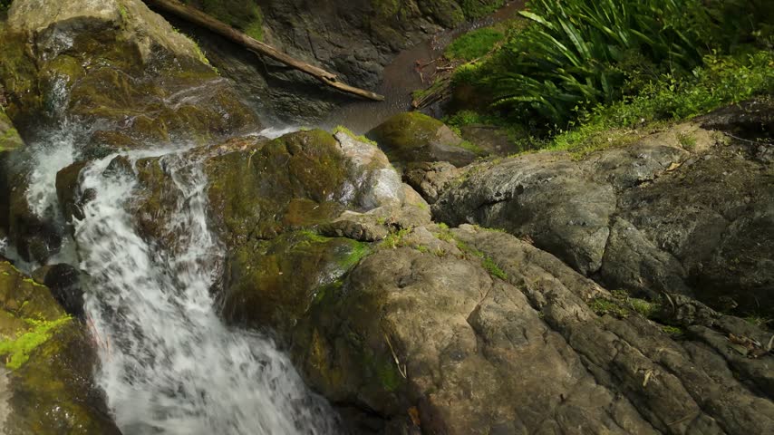 Aerial top down orbit reveals cascading Rainbow Falls waterfall flowing over mossy rocks in Tobago rainforest Caribbean island