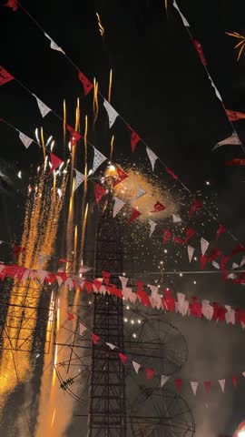 Pyrotechnic castle erupts with spinning aerial fireworks during traditional religious festival at night, vertical