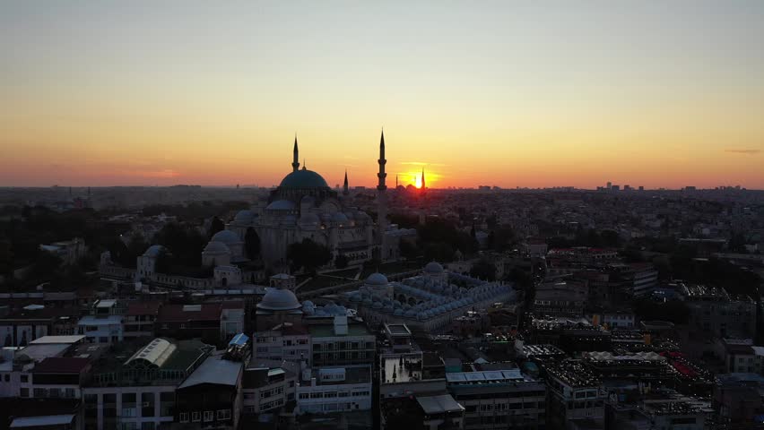 Breathtaking aerial drone view of the famous Suleymaniye Mosque silhouetted against a golden orange sky as the sun sets over the historic city of Istanbul, Turkey.