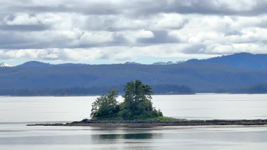 View of small island and mountains in Alaska with clouds in the sky and water reflecting the landscape