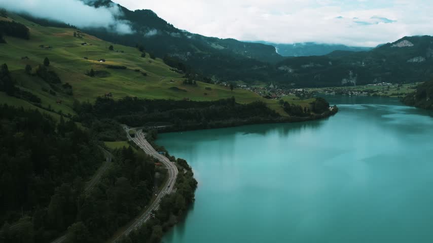 High-angle drone shot of a highway curving along Lake Lungern in the Swiss Alps.