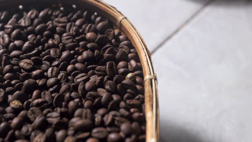 Detailed slow motion tracking shot showcasing rich textured brown coffee beans freshly roasted inside a rustic handmade basket. Smooth slow motion 50 percent footage of premium organic coffee beans displaying dark roasted textures inside a vintage wicker plate.