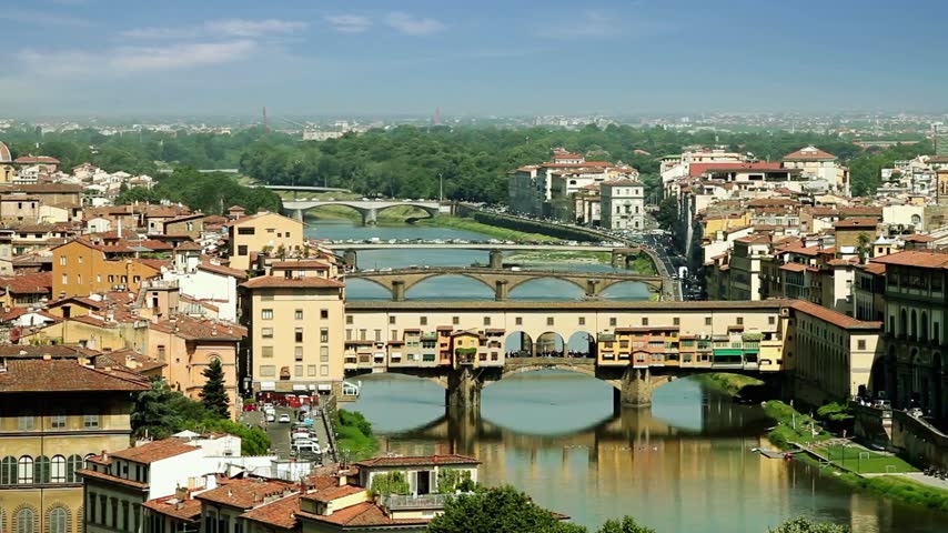 Cinematic moving footage of historic bridges across the Arno River in Florence, Italy, illuminated by natural sunlight, capturing the riverfront architecture, graceful bridge structures and distinctive Tuscan cityscape in an authentic travel scene.