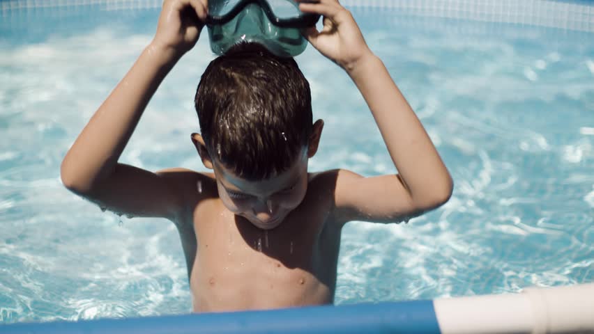 Little boy putting on goggles and diving into swimming pool during summer vacation