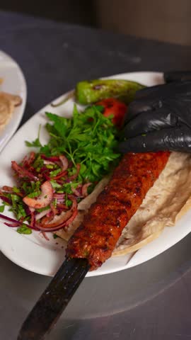 Chef Removing Adana Kebab from Skewer onto Plate