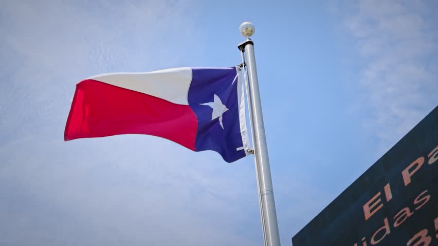 Footage of the Texas state flag featuring a vertical blue field with a white star and horizontal white and red bars waving against a clear sky.