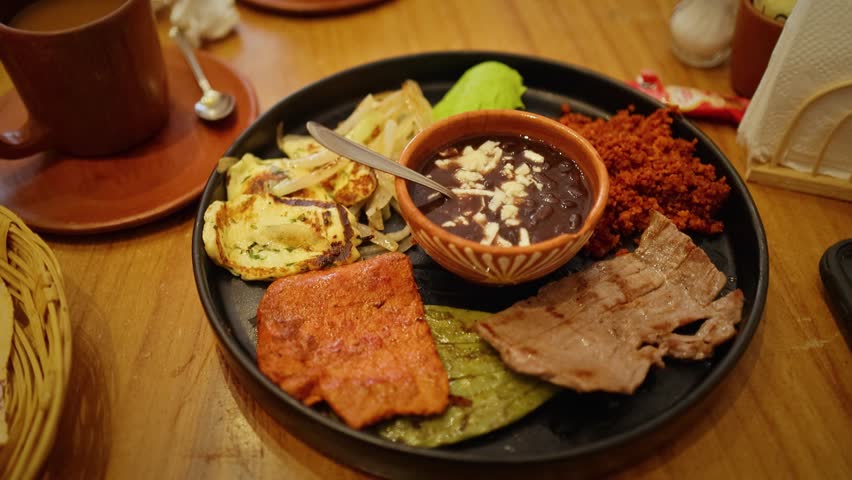 A close up of a traditional Mexican breakfast plate featuring chorizo, grilled beef, beans with cheese, nopal, and fresh cheese quesadillas.