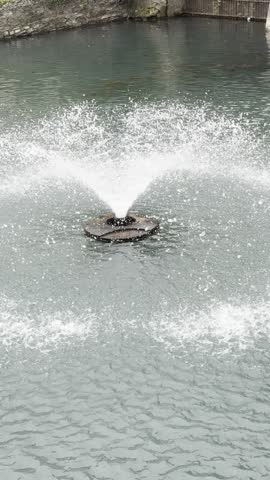 Park Fountain Water Jet Spraying into Pond, Rippling Surface Close Up
