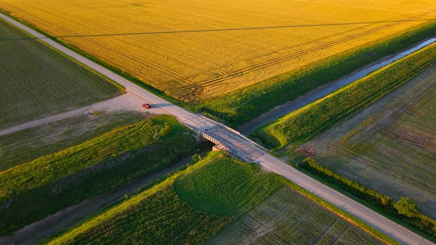 Aerial view of a single car at cross roads in the middle of fields  in a rural landscape of michigan during sunset.