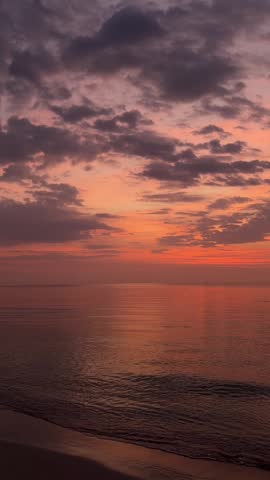 Vertical view of a serene ocean at dusk under a warm orange and purple cloudy sky.