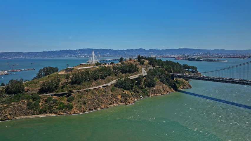 Dynamic aerial drone footage captures Yerba Buena Island landscape surrounded by San Francisco Bay waters featuring modern highway infrastructure and Bay Bridge connectivity.