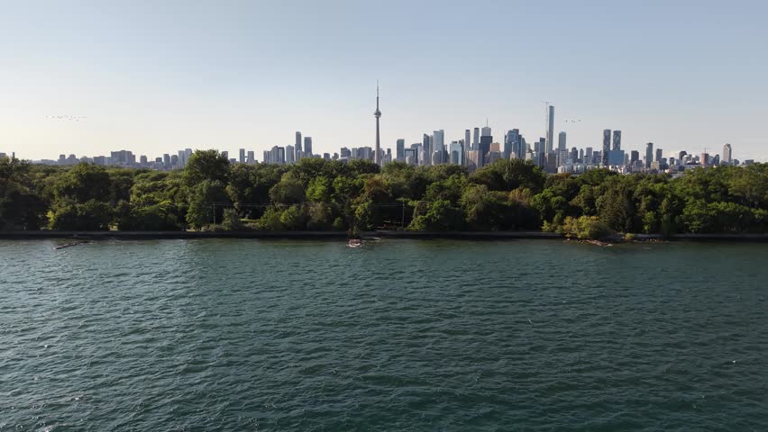 Aerial view ascending over the water and lush green trees of Toronto Islands, revealing the iconic downtown city skyline and CN Tower in the distance