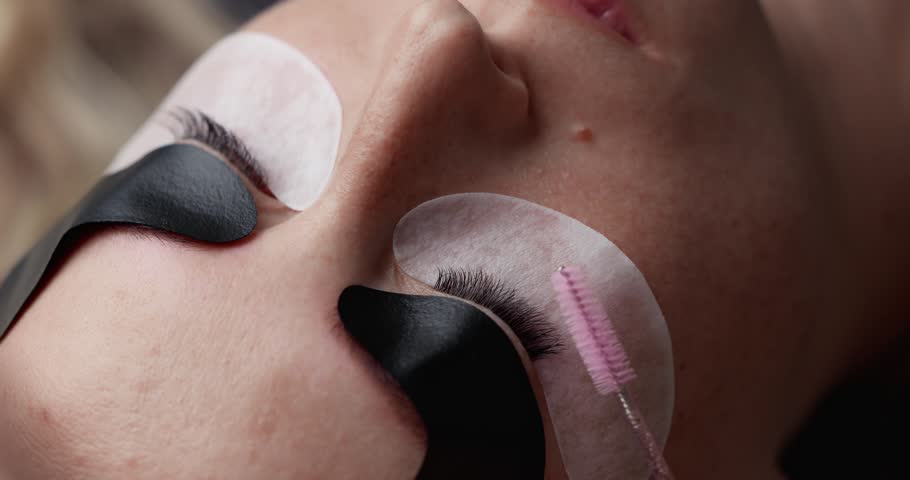 Slow motion close up of eyelash brushing and application during eyelash extension treatment in beauty studio.