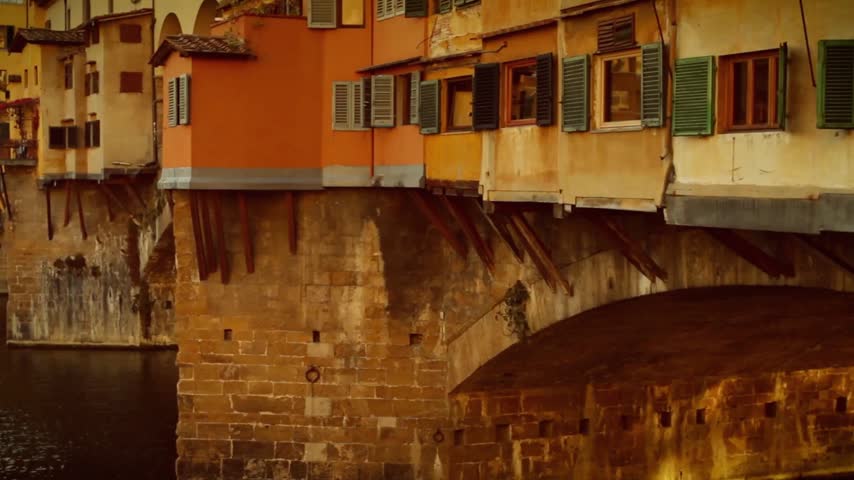 Horizontal HD video of Ponte Vecchio in Florence, Italy, at dusk, showing the historic bridge over the Arno River with cathedral architecture in the surrounding cityscape, capturing the atmospheric evening character of the Renaissance city.
