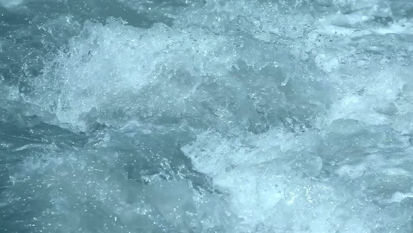 Churning rapids of rushing white water flowing rapidly through a turbulent mountain river stream with sparkling spray