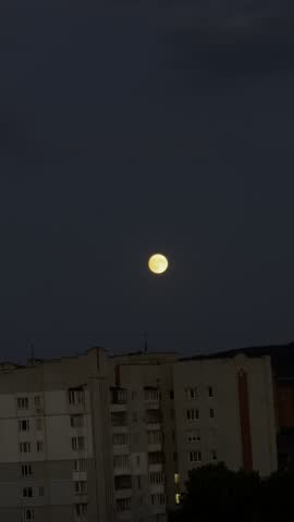Glowing yellow full moon shining in the dark night sky over a multi-story residential apartment building cityscape with copy space.