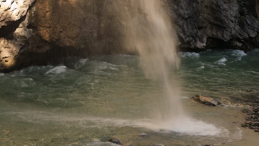Waterfall falling into the Aare river inside the Aare Gorge, Switzerland. Static shot of turquoise rapids, wet limestone walls and cascading water in Aareschlucht near Meiringen in summer