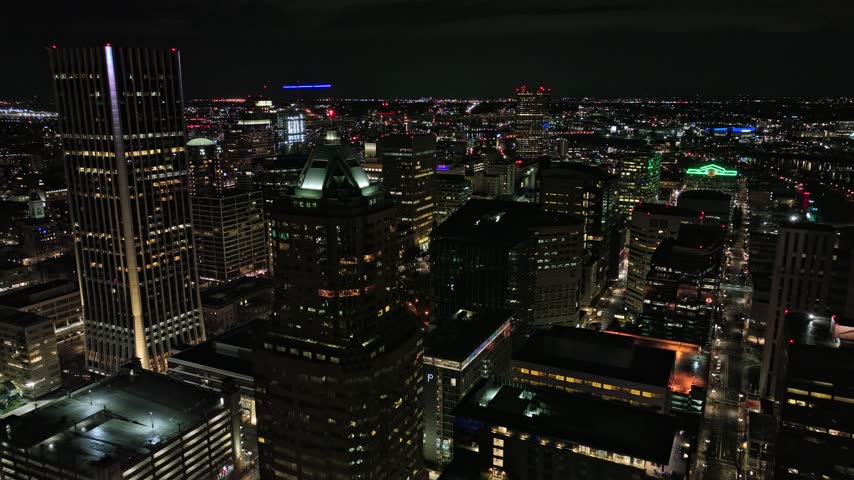 Cinematic aerial drone footage sweeping over Portland Oregon downtown district at night showcasing glowing skyscrapers urban infrastructure traffic light trails and expansive cityscape horizon line.