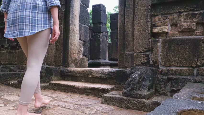 Barefoot woman walking up stone stairs entering ancient Nalanda Gedige temple in Sri Lanka