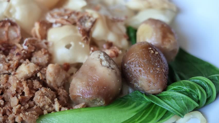 Close up shot of delicious Indonesian chicken noodles served with crispy wontons, seasoned minced chicken, green bok choy, and savory braised quail eggs in a white ceramic bowl.
