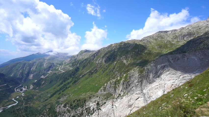 Dramatic high-altitude Alpine valley with winding mountain roads, rocky slopes and a cascading mountain stream in Switzerland.