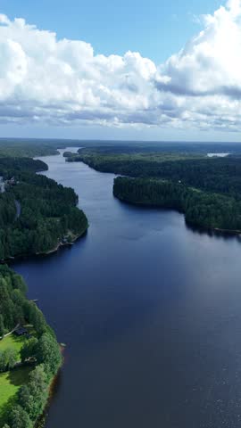 Vertical screen aerial view of a calm Finnish lake surrounded by thick woodland and rocky shoreline creating a peaceful Nordic summer landscape