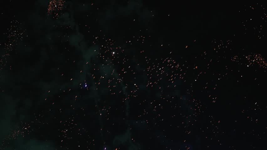 Spectacular fireworks explode across the night sky, sending bright colorful rockets and showers of glowing sparks upward through clouds of smoke. The dynamic display creates a festive atmosphere