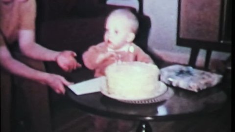A cute little one year old boy tries so hard to blow out the candle on his birthday cake in 1965.