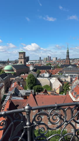 Vertical panoramic view overlooking historic Copenhagen rooftops, traditional red-tiled buildings, and cathedral spires on a sunny summer day.