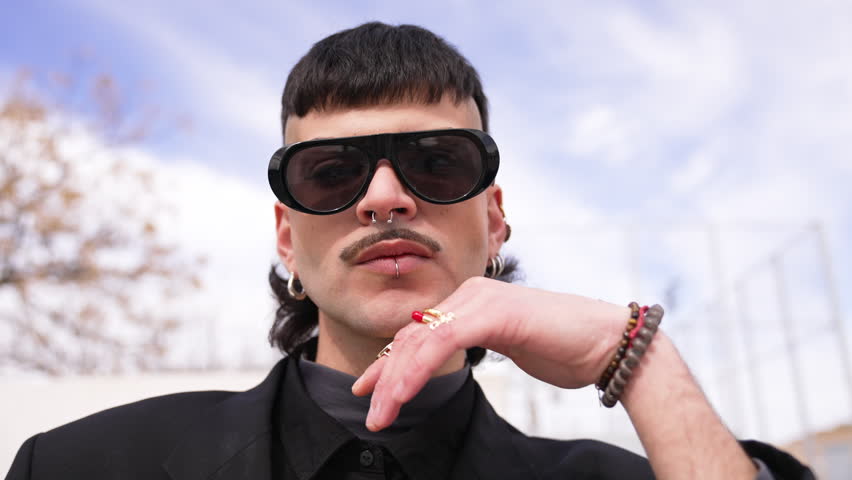 Zoom out on a portrait of a young man wearing glasses outdoors, looking at the camera