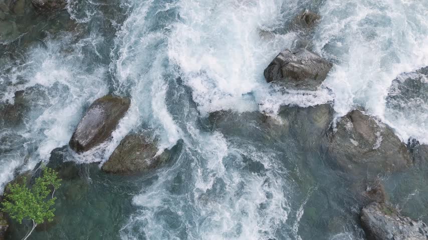 Aerial top down shot of wild river rapids splashing over rocks. Crystal clear blue running water cascading through a rocky streambed in a beautiful pristine nature landscape