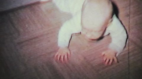 A cute baby boy learns to crawl on the living room floor with the help of his mother in 1964.