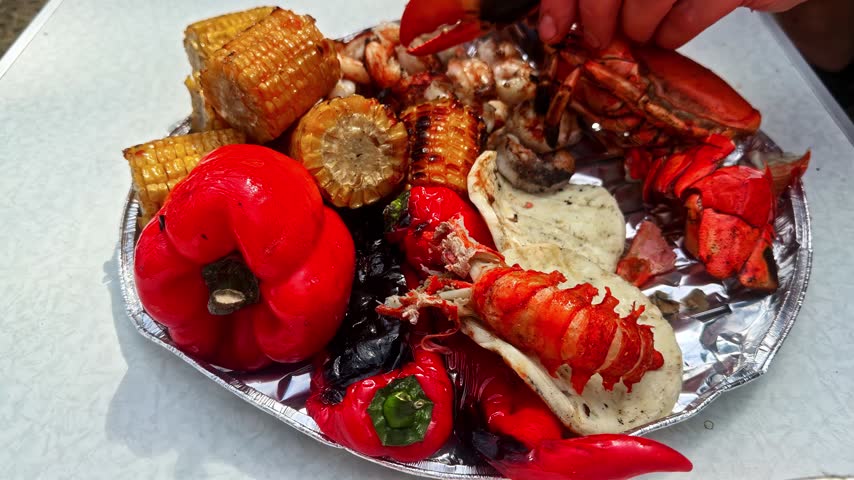 Eating Seafood Boil With Lobster, Red Peppers, Prawns And Corn OnThe Cob. - closeup shot