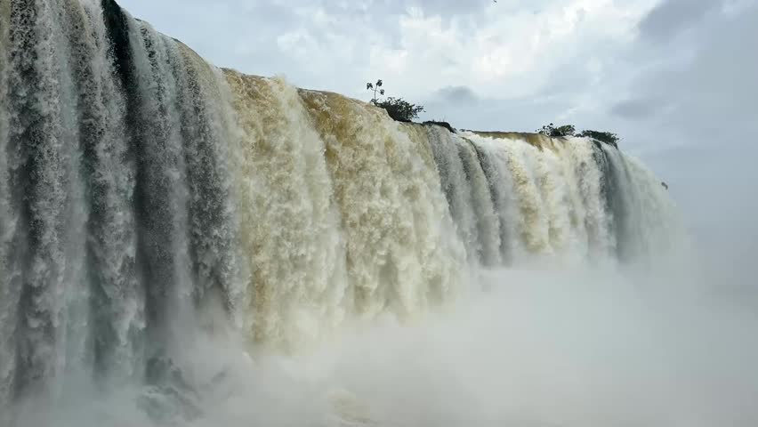Majestic Iguazu Falls in Brazil with powerful water cascades and misty spray under a cloudy sky