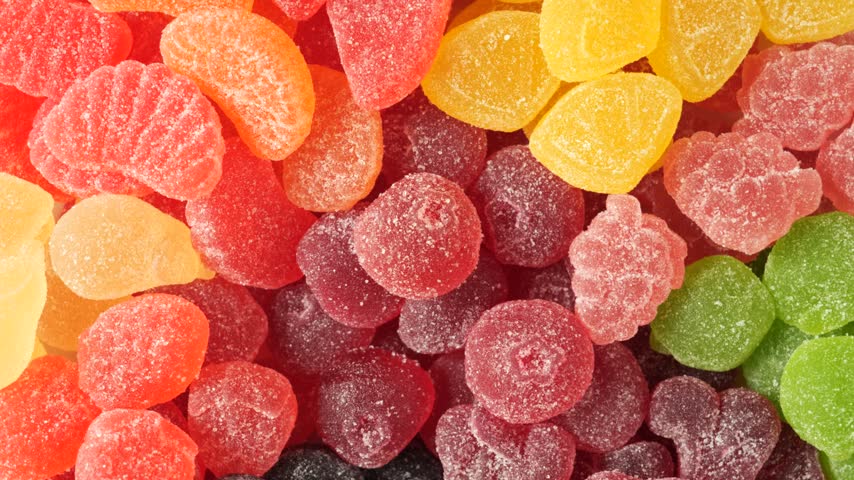Assortment of sweet and sour fruit-shaped gummy candies covered in sugar rotating in a top view