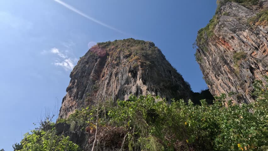 Wide shot of two huge overhanging cliffs covered with trees and bushes on Kolipe Island, surrounded by dense forest under a clear blue sky on a sunny morning.
