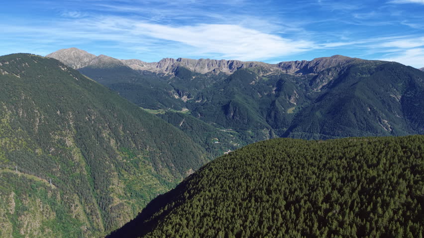 Sweeping Pyrenees mountain landscape in Andorra with dense forested slopes, deep valleys and rocky peaks under a partly cloudy blue sky