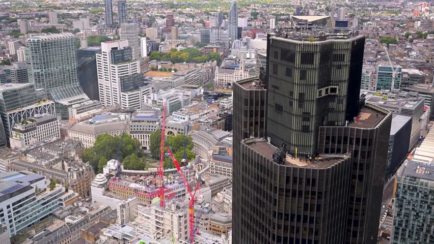 Tower 42 dominates the frame as the camera looks across a dense city skyline with cranes and rooftops below.