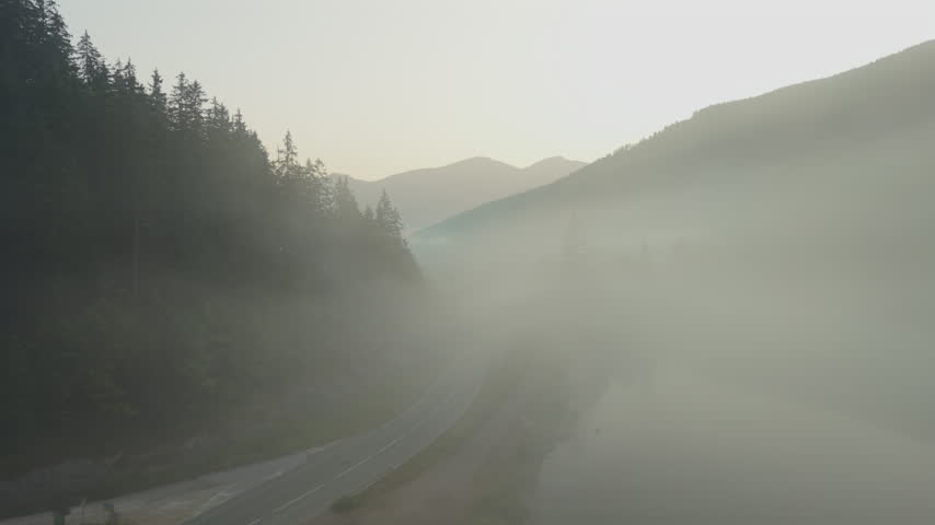 Foggy morning over a winding mountain road and mist-covered valley, aerial view.