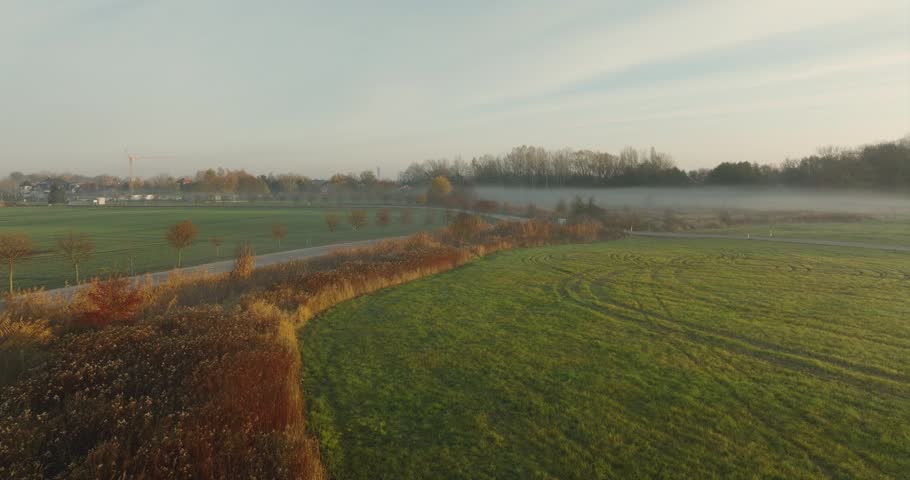 Aerial view of a winding road through agricultural fields shrouded in morning mist during a golden sunrise