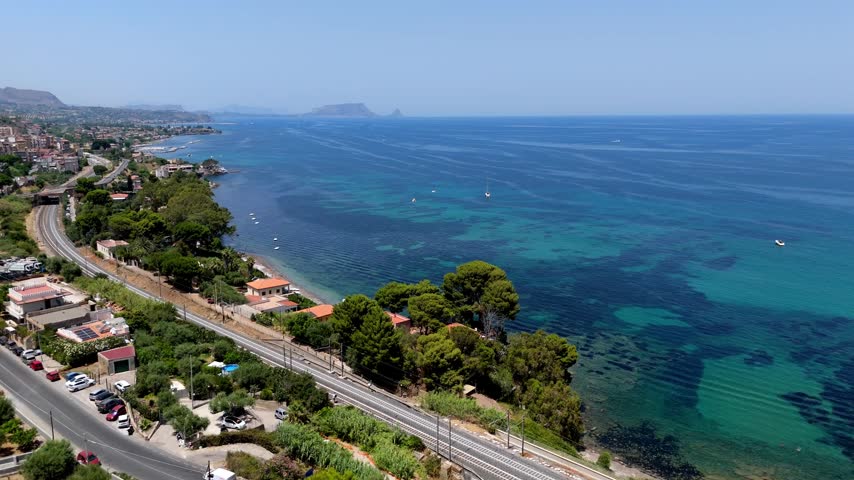 Daytime aerial view of the rocky coastline, crashing waves, and clear sea near Palermo in Sicily, Italy